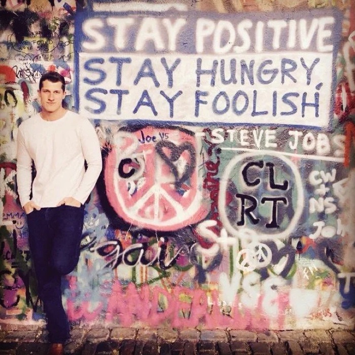 Jesse Henry in Prague, next to a wall reading Stay Hungry Stay Foolish